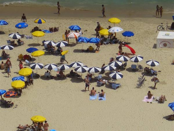 Crowded beach with yellow and blue umbrellas, bathers on light sand