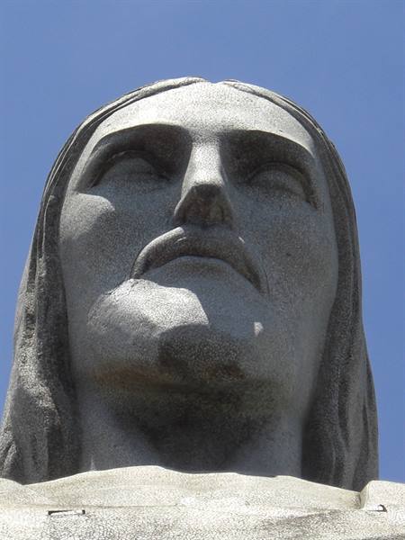 Stone face of Christ the Redeemer statue, Rio de Janeiro, against blue sky