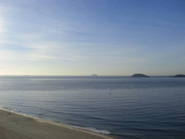 Sandy beach with gentle waves, islands on calm bay under hazy sky