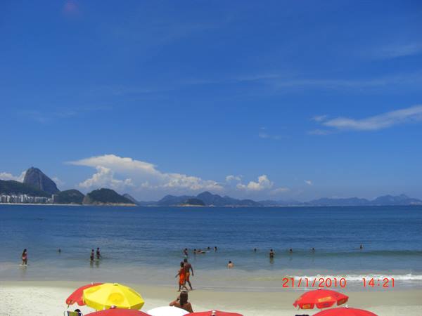 Beachgoers at Copacabana, red and yellow umbrellas, Sugarloaf Mountain in the distance