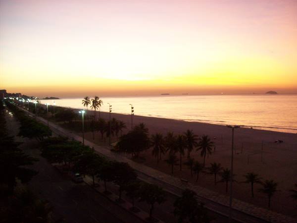 Palm trees and streetlights along the beach at dawn, calm sea, orange sky