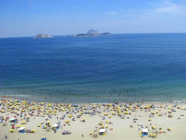 Crowded beach with yellow umbrellas, swimmers in the sea, islands on the horizon: Rio de Janeiro