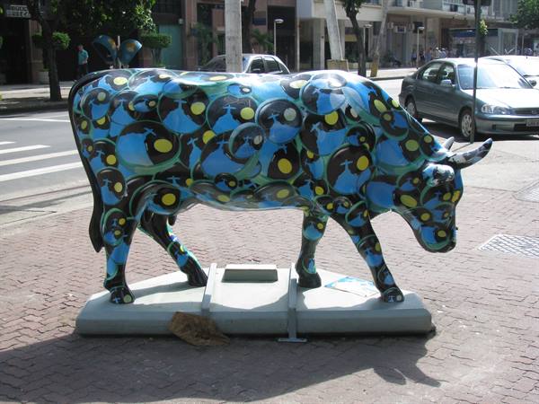 Sculpted cow painted blue with yellow patterns, displayed on a city sidewalk