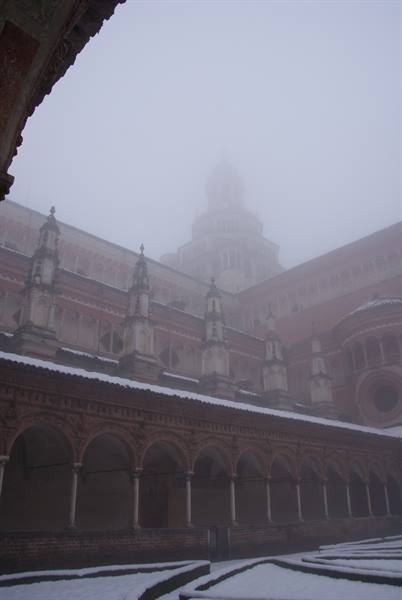 Certosa di Pavia in the fog: brick cloister arches with snow