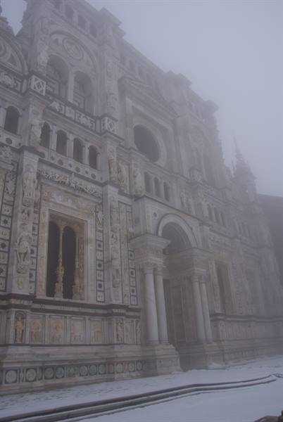 Marble facade of Certosa di Pavia wrapped in fog, snow on the ground