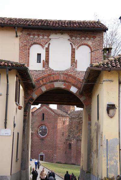 Brick arch over the street, people walking toward the abbey with rose window