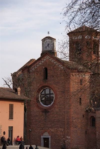 Medieval red-brick church with round window and clock, people sitting outside