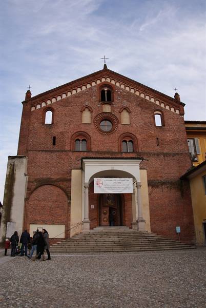 Red brick church with stepped gable facade, staircase and passersby under cloudy sky
