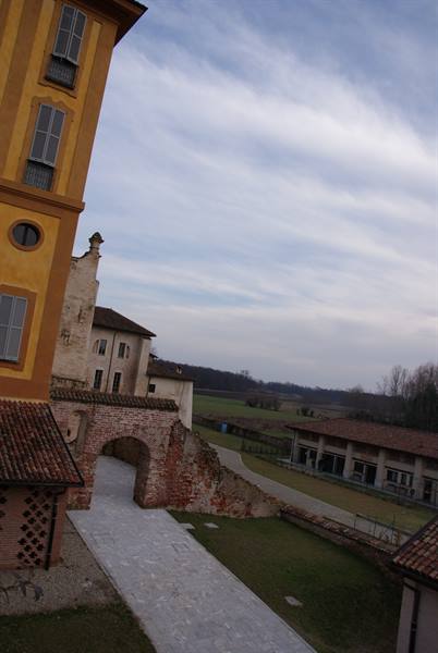 Old brick arch beside ochre facade, open fields under cloudy sky