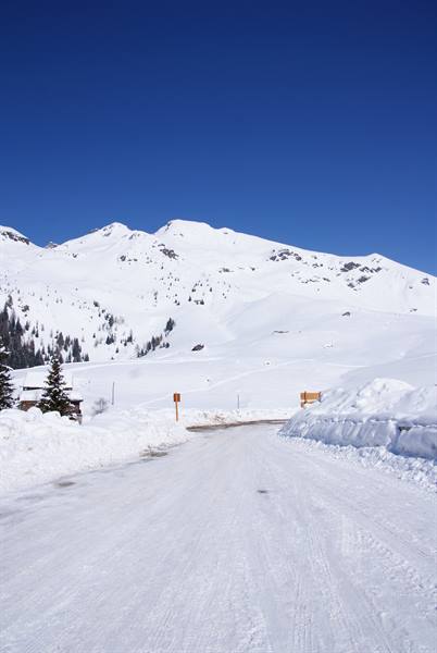 Snow-covered road between high snowbanks and snow-capped mountains