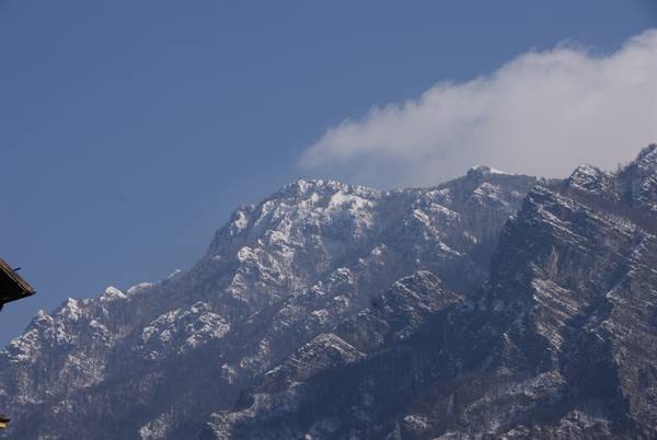Snow-dusted rocky peaks under blue sky, cloud on ridge, wooden roof edge