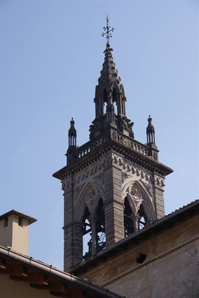 Gothic stone bell tower with spire and iron cross above rooftops