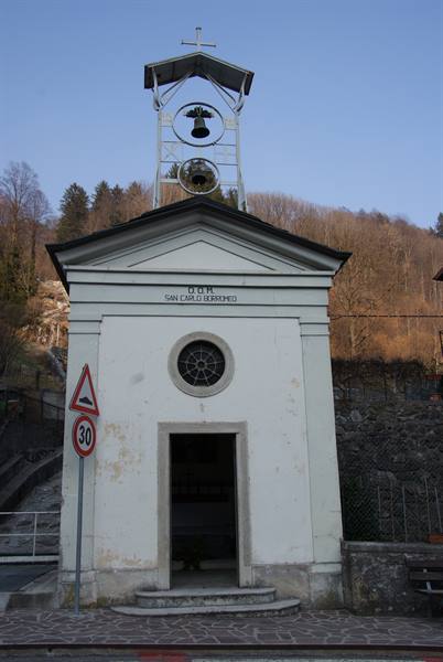 Small white church of San Carlo Borromeo with metal bell tower among bare woods