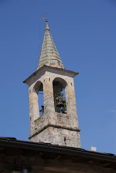 Stone bell tower with green shingle spire and bells, blue sky