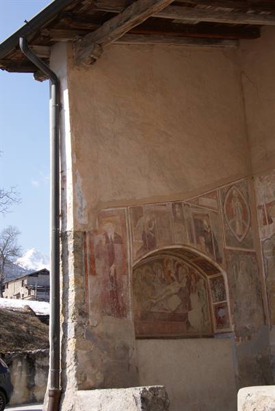 Faded medieval frescoes on a church outer wall, snowy mountain behind