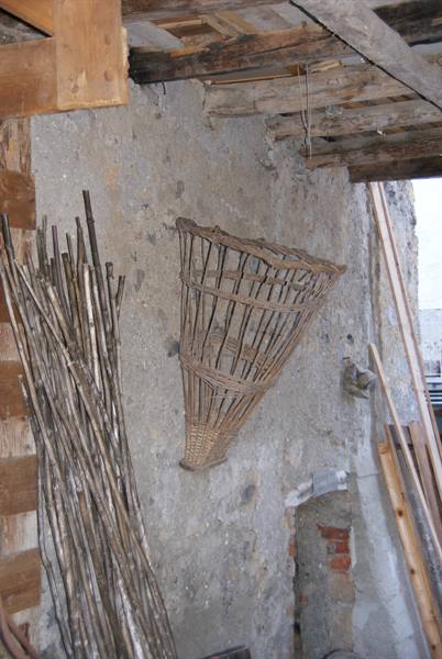 Wicker basket hanging on rustic wall among wooden sticks inside a barn