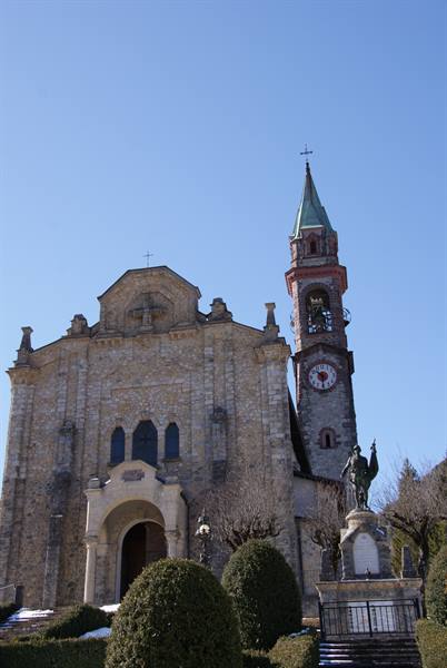 Stone church with clock bell tower and statue under clear blue sky