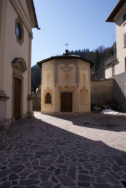 Octagonal frescoed chapel with cross, between sacred buildings, on stone pavement