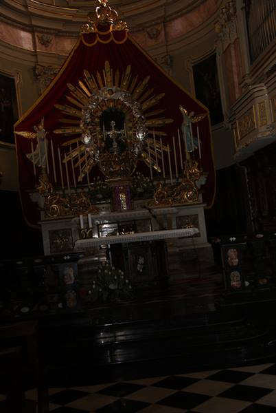 Marble high altar with golden cross and red canopy inside a dim church