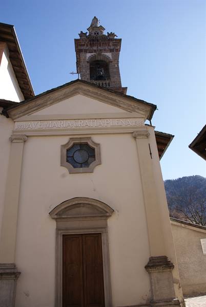 Church facade with Ave Maria inscription, stone bell tower and mountain behind