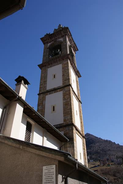 Stone and white plaster bell tower under blue sky, mountain behind rooftops