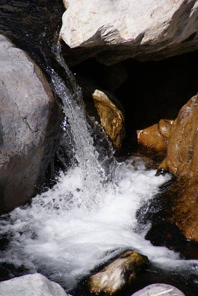 Water cascading foamy between gray boulders and sunlit ochre rocks