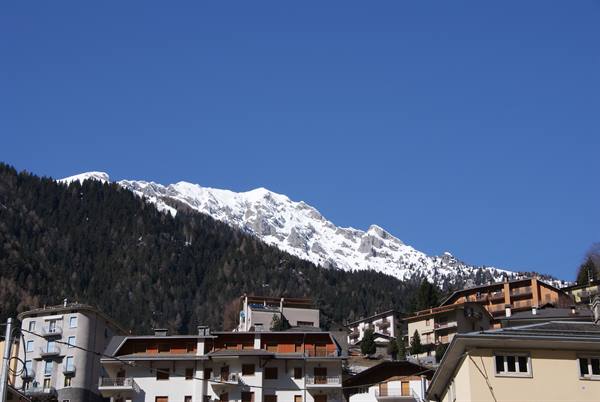 Village of wooden and plastered buildings beneath snowy peaks and clear blue sky