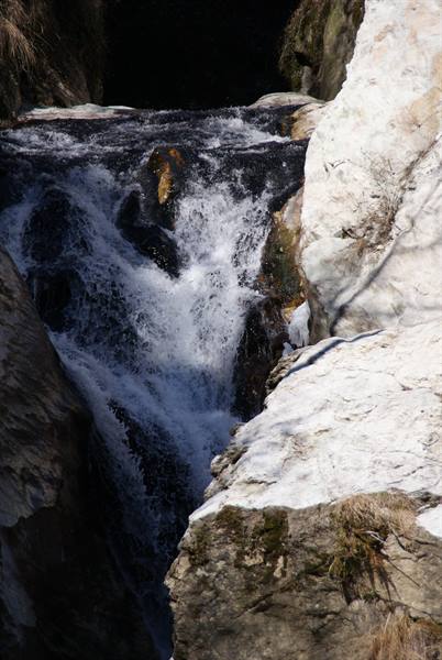 Waterfall rushing between mossy snow-dusted rocks in bright sunlight