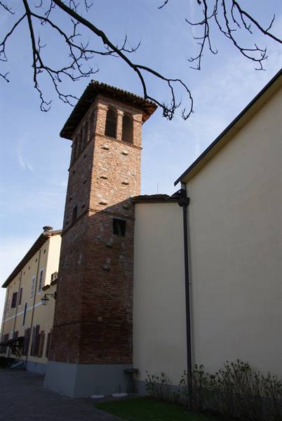 Brick bell tower between yellow buildings, bare branches, blue sky