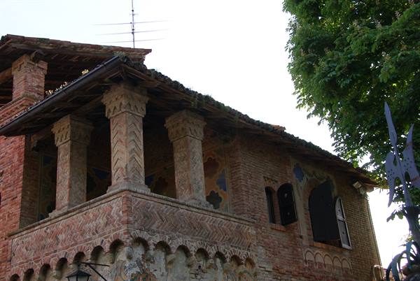 Medieval brick house with decorated loggia columns, green trees nearby