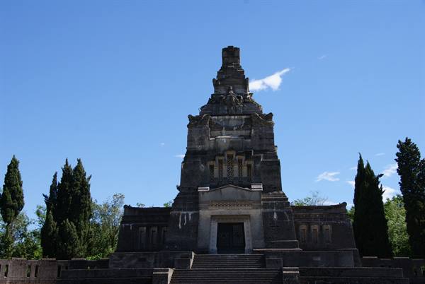 Gray stone monument with staircase, cypress trees alongside, blue sky