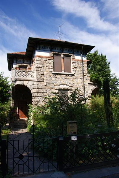 Stone villa with balcony and arches, partially hidden by greenery