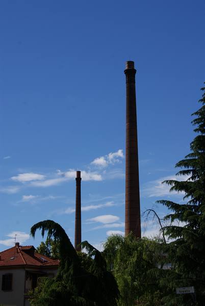 Two brick chimneys rise above trees and rooftops under blue sky
