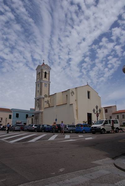 Church with bell tower by the square, parked cars and pedestrians under scattered clouds