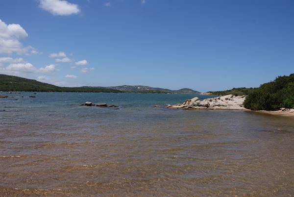 Clear shallow water over granite rocks, green shrubs on the right, hills in the distance