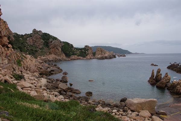 Granite boulders frame a calm turquoise cove with green shrubs under cloudy skies
