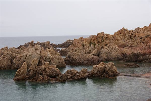 Pink granite rocks in green sea, grey sky, soft diffused light