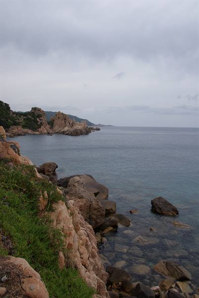Pink granite rocks over turquoise sea under cloudy sky