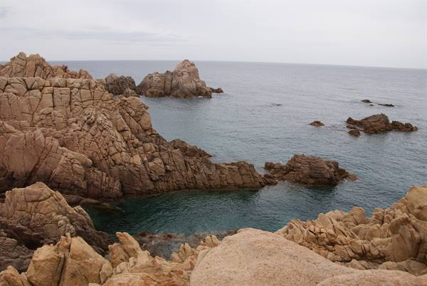 Pink granite cliffs plunging into turquoise coves under grey sky
