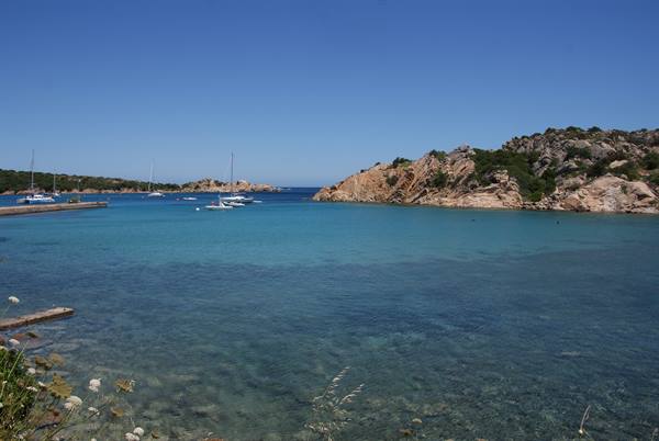 sailboat and dinghies in turquoise water among granite rocks and Mediterranean scrub