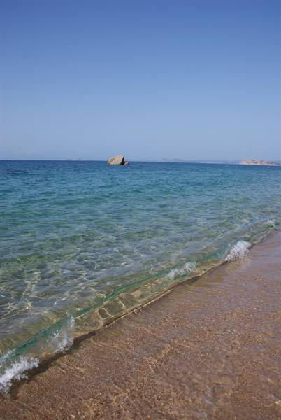 Clear turquoise water over sandy beach, rock in the distance