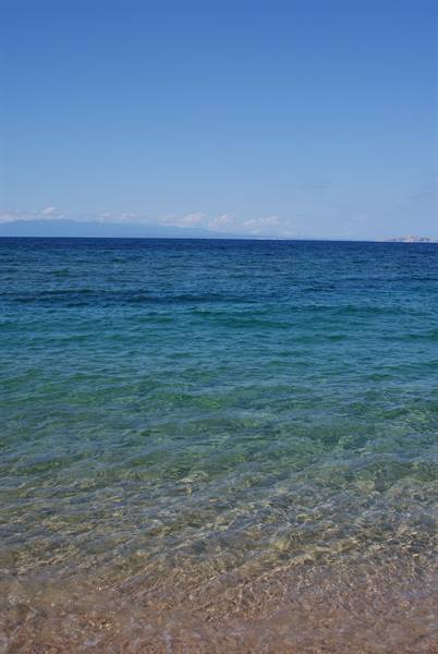 Clear turquoise water over sand, blue sky and distant islands on the horizon
