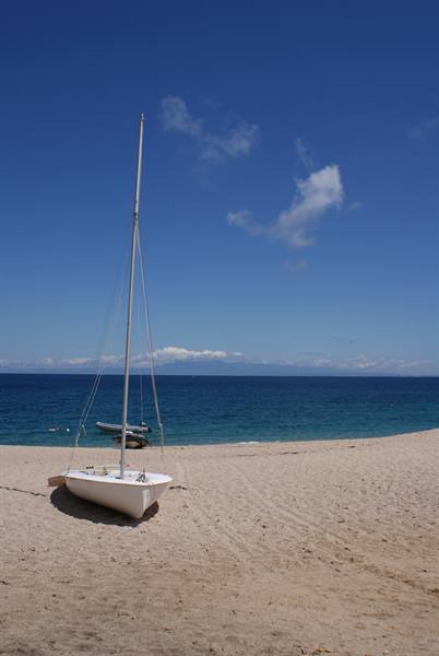 White sailboat beached on the sand in front of the blue sea