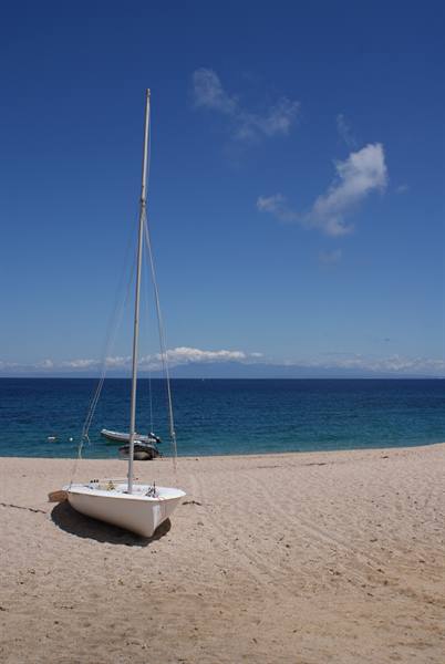 White sailboat beached on the sand in front of the blue sea