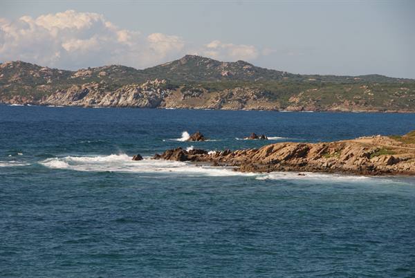 Granite rocks and waves on blue sea, green Mediterranean scrub on Sardinian hills