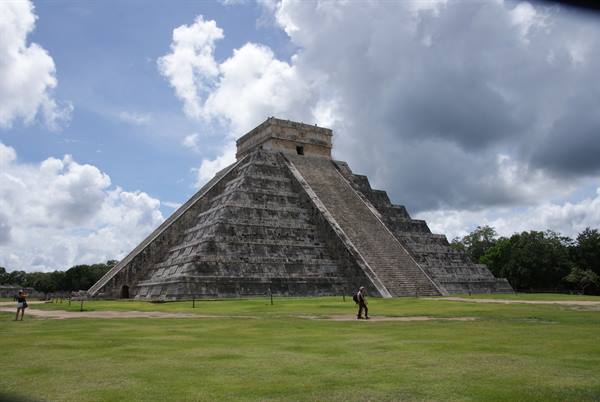 El Castillo pyramid at Chichén Itzá, stepped stone, tourists on green lawn, cloudy sky