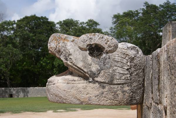Stone serpent head carving at Chichén Itzá, with green trees behind