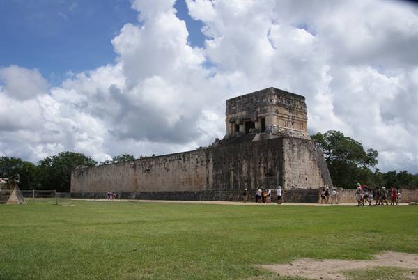 Tourists walk beside the Great Ball Court at Chichén Itzá under white clouds