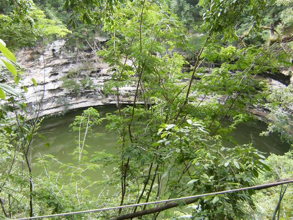 Sacred Cenote at Chichén Itzá: dark green water between rocky cliffs and trees