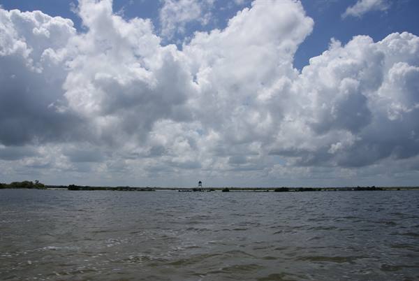 White clouds over choppy water, small tower and trees on distant shore